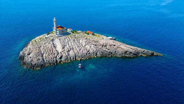 Aerial view of Blitvenica Lighthouse on a small rocky island surrounded by the deep blue Adriatic Sea with a small boat anchored nearby Zirje Sibensko kninska zupa Croatia. Aerial view of Blitvenica Lighthouse on a small rocky island surrounded by the deep blue Adriatic Sea with a small boat anchored nearby Zirje Sibensko kninska zupa Croatia.