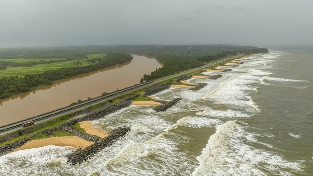 Aerial view of Maravanthe beach with a road running between the sea and river featuring rocky breakwaters and lush green surroundings in Maravanthe Karnataka India. Aerial view of Maravanthe beach with a road running between the sea and river featuring rocky breakwaters and lush green surroundings in Maravanthe Karnataka India.