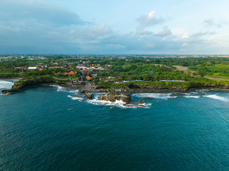 Aerial view of Tanah Lot Temple situated on a rocky outcrop surrounded by the Indian Ocean with lush green coastal landscape and traditional Balinese architecture in Kecamatan Kediri Bali Indonesia. Aerial view of Tanah Lot Temple situated on a rocky outcrop surrounded by the Indian Ocean with lush green coastal landscape and traditional Balinese architecture in Kecamatan Kediri Bali Indonesia.