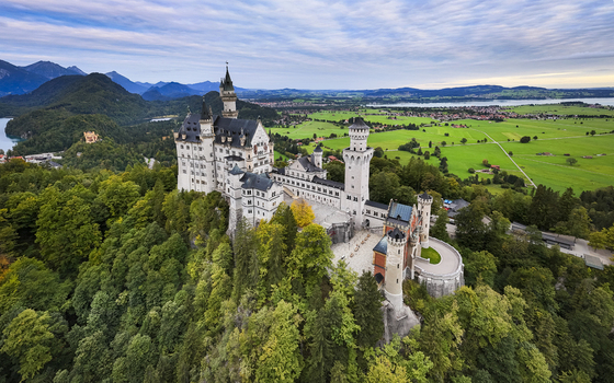 Aerial view of the majestic Neuschwanstein Castle perched atop a hill a symphony of grey stone against the verdant forest Füssen Bayern Germany. Aerial view of the majestic Neuschwanstein Castle perched atop a hill a symphony of grey stone against the verdant forest Füssen Bayern Germany.