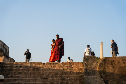 Sri Lanka 24 January 2026 View of Buddhist monks in traditional robes and tourists walking up ancient stone stairs against a clear blue sky.