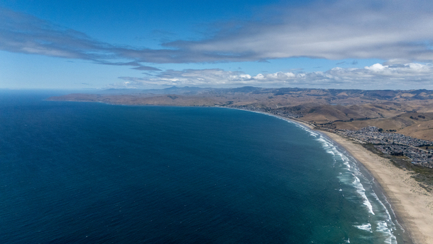 Aerial view of the coastline featuring a long sandy beach rolling hills and the deep blue waters of the Pacific Ocean in Morro Bay California United States.