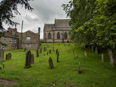 View of St Margaret s Church and its historic graveyard in Yorkshire with weathered stone headstones lush green grass and stone buildings in Hawes England United Kingdom. View of St Margaret s Church and its historic graveyard in Yorkshire with weathered stone headstones lush green grass and stone buildings in Hawes England United Kingdom.