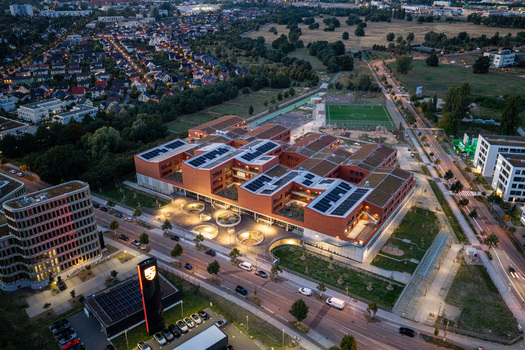 Berlin Germany 07 September 2026 Aerial view of the New School Campus in Adlershof Eisenhutweg featuring modern red brick buildings green roofs with solar panels and illuminated courtyards.