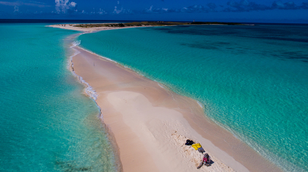 Aerial view of Los Roques archipelago featuring a white sandbar surrounded by turquoise waters with a person resting on the shore in Los Roques Dependencias Federales Venezuela. Aerial view of Los Roques archipelago featuring a white sandbar surrounded by turquoise waters with a person resting on the shore in Los Roques Dependencias Federales Venezuela.