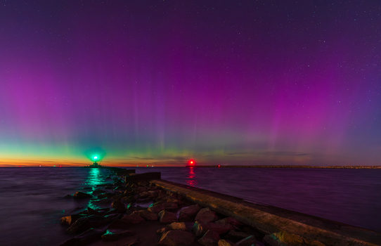 View of the aurora borealis illuminating the night sky above the breakwater and lighthouse at Gorki Zachodnie on the Baltic Sea in Gdansk Pomeranian Voivodeship Poland.