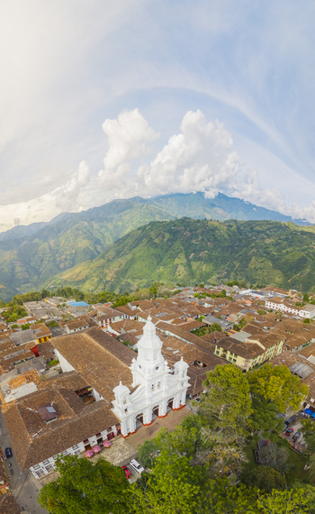 Aerial view of a bright white church steeple piercing the skyline amidst terracotta roofs with verdant mountains looming in the backdrop Salamina Caldas Colombia.