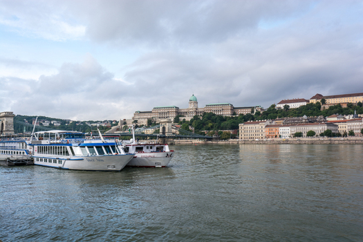 View of Buda Castle overlooking the Danube River with river cruise ships docked along the bank in Budapest Hungary.