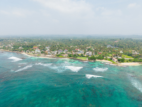 Aerial view of Devil s Rock and the turquoise coastline with surfers in the waves and lush palm trees in Ahangama Southern Province Sri Lanka. Aerial view of Devil s Rock and the turquoise coastline with surfers in the waves and lush palm trees in Ahangama Southern Province Sri Lanka.
