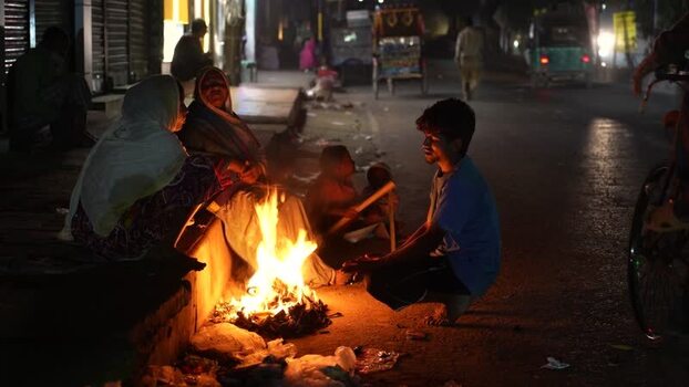 View of people sitting around a fire on a street at night Bangladesh.