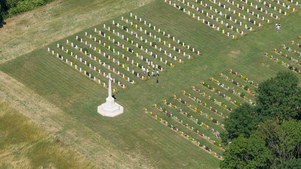 Aerial view of the Thiepval Anglo French Cemetery with rows of white headstones a central Cross of Sacrifice and visitors walking through the grass in Thiepval Hauts de France France.