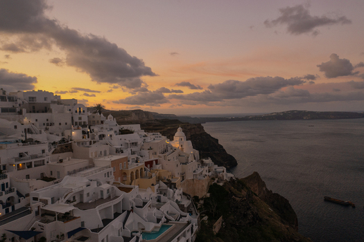 Aerial view of the whitewashed buildings cascade down the cliffs towards the Aegean Sea as the sun sets painting the sky with hues of orange and purple Fira Thira Greece. Aerial view of the whitewashed buildings cascade down the cliffs towards the Aegean Sea as the sun sets painting the sky with hues of orange and purple Fira Thira Greece.