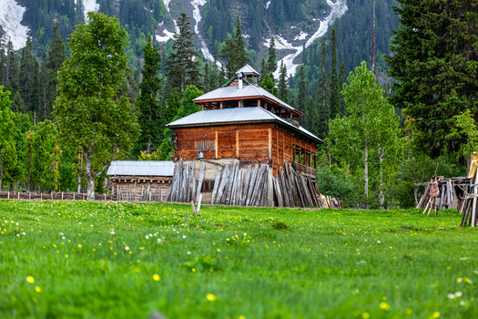 View of a traditional wooden house in a lush green meadow surrounded by tall trees and snow capped mountains in Arang Kel Azad Kashmir Pakistan. View of a traditional wooden house in a lush green meadow surrounded by tall trees and snow capped mountains in Arang Kel Azad Kashmir Pakistan.
