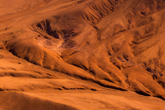 Aerial view of the rugged arid landscape of the Atacama Desert with deep gullies and shadows cast across the reddish brown terrain in Antofagasta Chile.