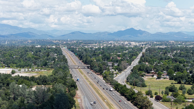 Aerial view of Interstate 5 highway passing through Redding with surrounding trees suburban neighborhoods and distant mountains under a cloudy sky in Redding California United States. Aerial view of Interstate 5 highway passing through Redding with surrounding trees suburban neighborhoods and distant mountains under a cloudy sky in Redding California United States.