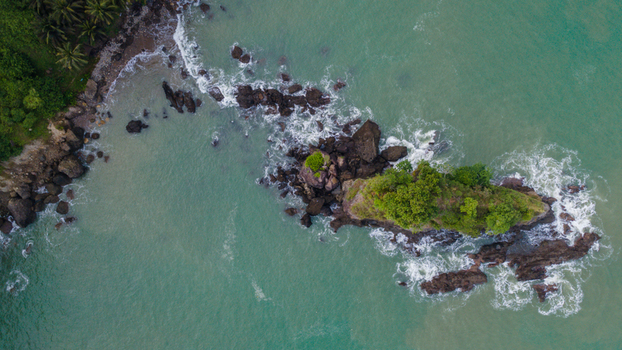 Aerial view of Pantai Karang Agung featuring a rocky outcrop with lush vegetation surrounded by turquoise sea waves in Ayah Central Java Indonesia. Aerial view of Pantai Karang Agung featuring a rocky outcrop with lush vegetation surrounded by turquoise sea waves in Ayah Central Java Indonesia.