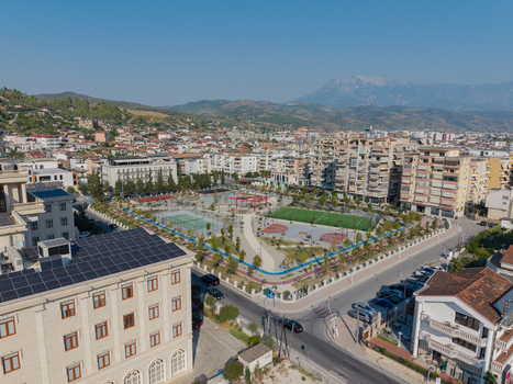 Aerial view of a modern sports park featuring a soccer field and basketball court surrounded by urban buildings and distant mountains in Berat Berat County Albania.
