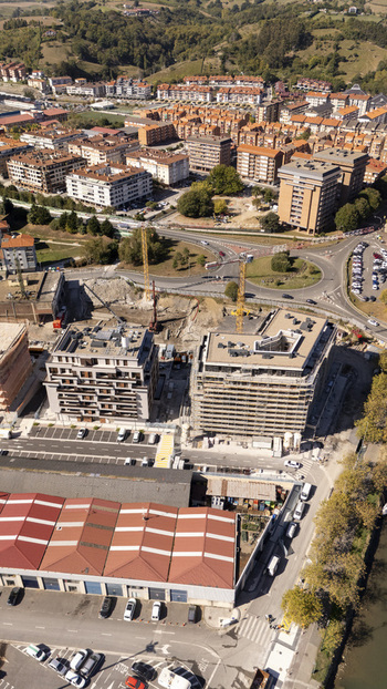 Aerial view of a construction site with two new apartment buildings and cranes surrounded by residential housing a roundabout and industrial buildings in Zumaia Basque Country Spain.
