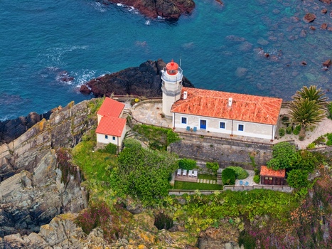 Aerial view of the Faro de Cudillero lighthouse with its red tiled roof and white tower perched on rocky cliffs overlooking the blue sea in Cudillero Asturias Spain. Aerial view of the Faro de Cudillero lighthouse with its red tiled roof and white tower perched on rocky cliffs overlooking the blue sea in Cudillero Asturias Spain.