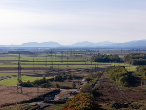 Aerial view of high voltage power lines and electricity pylons crossing agricultural fields and rural landscape with mountains in the distance Slovenia.