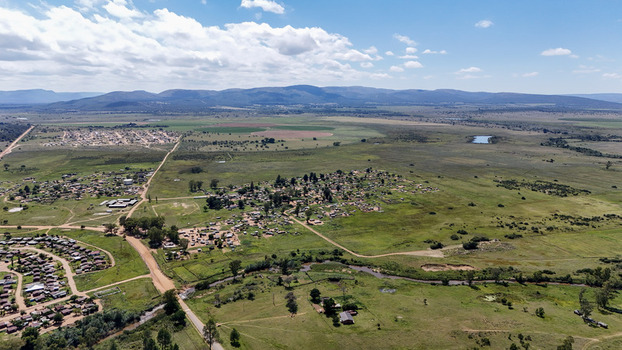 Aerial view of the Alma settlement featuring scattered houses and dirt roads across green plains with distant mountains in Waterberg District Municipality Limpopo South Africa. Aerial view of the Alma settlement featuring scattered houses and dirt roads across green plains with distant mountains in Waterberg District Municipality Limpopo South Africa.