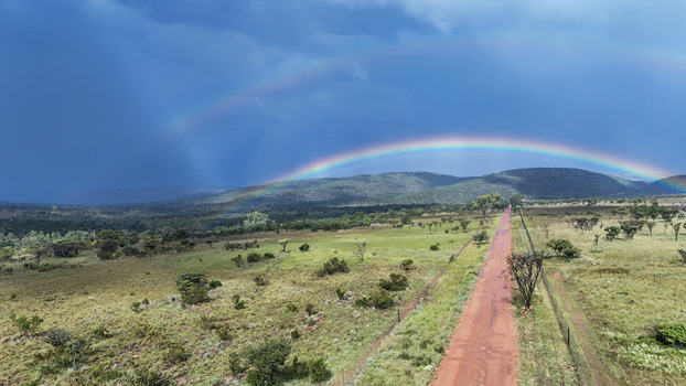 Aerial view of a red dirt road stretching through the green savanna landscape under a double rainbow and dark stormy sky Waterberg District Municipality Limpopo South Africa. Aerial view of a red dirt road stretching through the green savanna landscape under a double rainbow and dark stormy sky Waterberg District Municipality Limpopo South Africa.