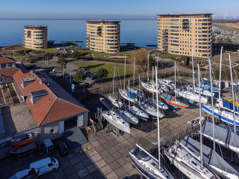 Aerial view of sailboats docked near low buildings with red roofs and cylindrical apartment towers against the blue sea Almere Netherlands. Aerial view of sailboats docked near low buildings with red roofs and cylindrical apartment towers against the blue sea Almere Netherlands.
