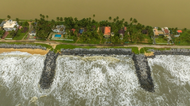 Aerial view of Mattu Beach featuring rocky breakwaters protecting the coastline with palm trees and residential houses along the shore in Udupi Karnataka India.