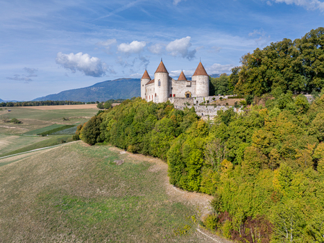Aerial view of Champvent Castle perched on a hill surrounded by lush green forests and rolling fields under a clear blue sky in Champvent Vaud Switzerland. Aerial view of Champvent Castle perched on a hill surrounded by lush green forests and rolling fields under a clear blue sky in Champvent Vaud Switzerland.
