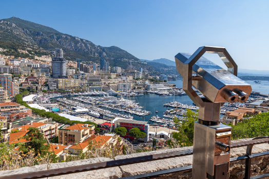 View of Port Hercules with luxury yachts modern buildings and hills in the background seen through a public coin operated telescope in Monaco City Monaco. View of Port Hercules with luxury yachts modern buildings and hills in the background seen through a public coin operated telescope in Monaco City Monaco.