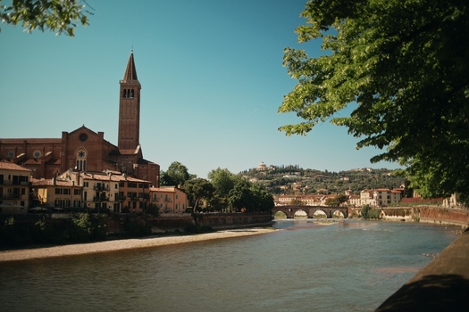 View of the Basilica of Santa Anastasia and historic buildings along the Adige River with the Ponte Pietra in the distance under a clear sky in Verona Veneto Italy.