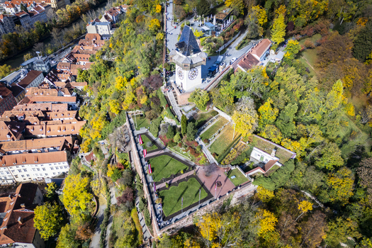 Aerial view of the iconic clock tower Uhrturm standing tall amidst a tapestry of autumnal hues perched atop Schlossberg hill Graz Styria Austria.