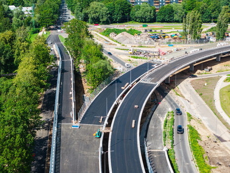 Aerial view of a new road construction project featuring a modern highway overpass with fresh asphalt surrounded by lush green trees and urban infrastructure in Riga Latvia. Aerial view of a new road construction project featuring a modern highway overpass with fresh asphalt surrounded by lush green trees and urban infrastructure in Riga Latvia.