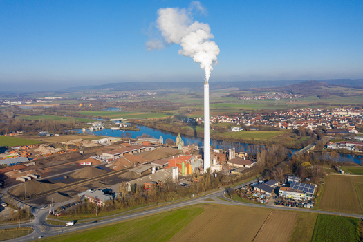 Aerial view of the Liapor GmbH Co. KG industrial plant with a tall chimney emitting white smoke near the river and fields in Hallerndorf Bayern Germany. Aerial view of the Liapor GmbH Co. KG industrial plant with a tall chimney emitting white smoke near the river and fields in Hallerndorf Bayern Germany.
