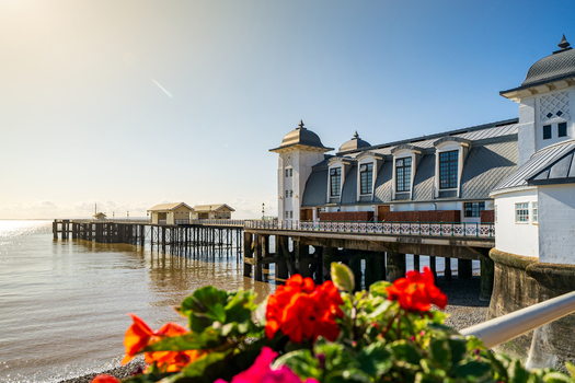 View of the historic Penarth Pier Pavilion with its Victorian architecture and red flowers in the foreground under a clear sky in Penarth United Kingdom. View of the historic Penarth Pier Pavilion with its Victorian architecture and red flowers in the foreground under a clear sky in Penarth United Kingdom.