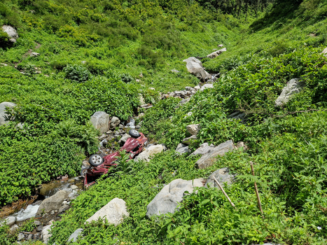 View of an overturned red car in a rocky stream bed surrounded by lush green vegetation in Malana Himachal Pradesh India.