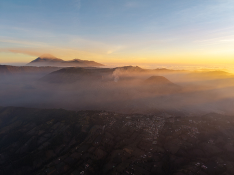 Aerial view of Cemorolawang village in the volcanic landscape of Mount Bromo at sunset with golden light over misty peaks and fields in Kecamatan Sukapura Jawa Timur Indonesia.