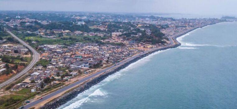 Aerial view of a coastal town featuring a long stretch of road running parallel to the rocky shoreline with residential buildings and lush vegetation Ghana. Aerial view of a coastal town featuring a long stretch of road running parallel to the rocky shoreline with residential buildings and lush vegetation Ghana.
