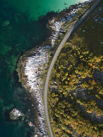 Aerial view of a winding coastal road along the rocky shoreline of Vik Strand with turquoise water and autumn foliage in Leknes Nordland Norway. Aerial view of a winding coastal road along the rocky shoreline of Vik Strand with turquoise water and autumn foliage in Leknes Nordland Norway.
