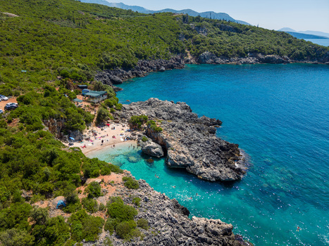 Aerial view of Aquarium Beach with turquoise waters rocky formations and lush green hills in Jala Vlore County Albania.