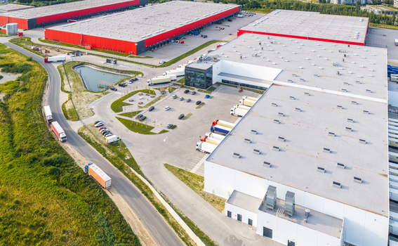 Aerial view of a large logistics park with expansive warehouse buildings loading docks semi trucks and a parking lot in Kowale Pomeranian Voivodeship Poland.