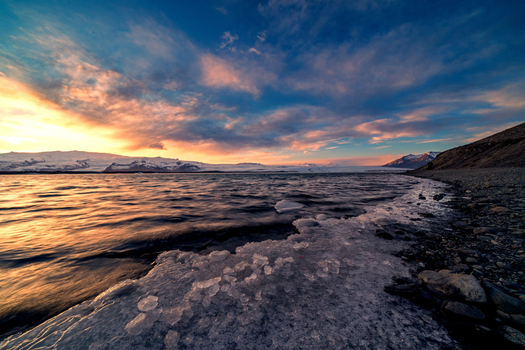 View of Jokulsarlon Glacier Lagoon with floating ice chunks and distant snow capped mountains under a vibrant sunset sky Sveitarfelagid Hornafjordur Iceland. View of Jokulsarlon Glacier Lagoon with floating ice chunks and distant snow capped mountains under a vibrant sunset sky Sveitarfelagid Hornafjordur Iceland.