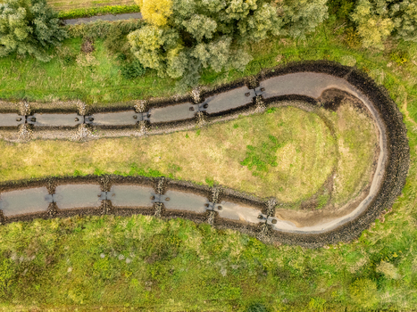 Aerial view of Sluis en stuwcomplex Hagestein featuring a fish ladder with stone lined banks surrounded by lush green vegetation in Hagestein Utrecht Netherlands.