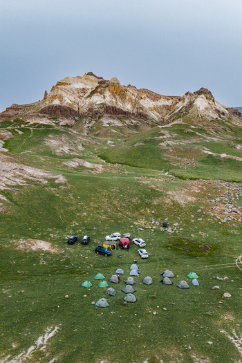 Aerial view of a campsite with colorful tents and parked vehicles nestled at the base of the scenic Airakty mountains in the grassy landscape of Shetpe Mangystau Region Kazakhstan.