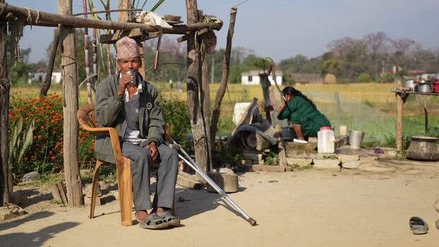 View of a man with a crutch sitting in a rural yard Nepal. View of a man with a crutch sitting in a rural yard Nepal.