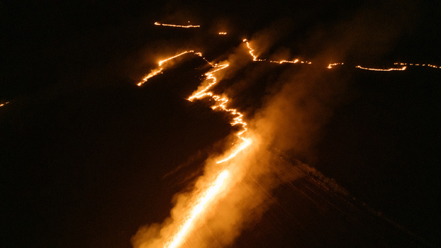 Aerial view of a night fire burning across a field with bright orange flames and smoke trails in Sremska Mitrovica Vojvodina Serbia.