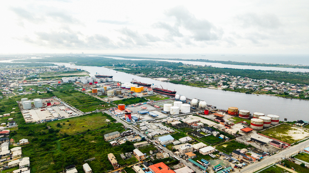 Aerial view of the industrial port area in Satellite Town with large storage tanks cargo ships docked in the river and surrounding urban development in Lagos Lagos Nigeria.