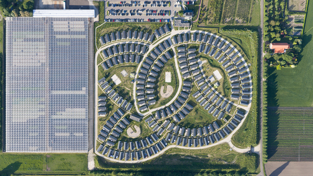 Aerial view of a modern residential neighborhood with a unique curved layout adjacent to a large glass greenhouse complex and surrounding agricultural fields in Venlo Limburg Netherlands. Aerial view of a modern residential neighborhood with a unique curved layout adjacent to a large glass greenhouse complex and surrounding agricultural fields in Venlo Limburg Netherlands.