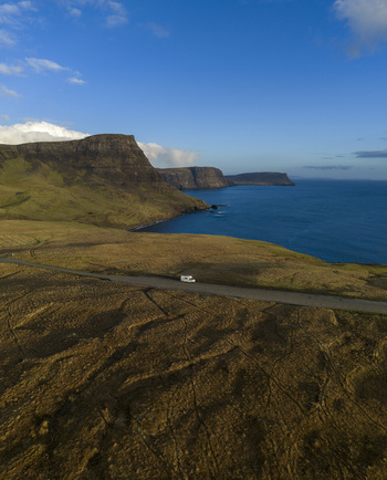 Aerial view of a white camper van parked on a coastal road overlooking dramatic cliffs and the blue sea in Isle of Skye. Aerial view of a white camper van parked on a coastal road overlooking dramatic cliffs and the blue sea in Isle of Skye.