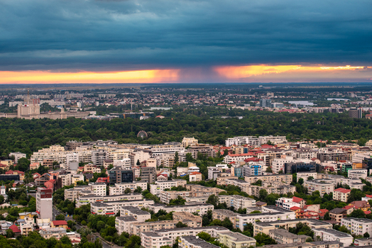 View of the Bucharest skyline under a dramatic stormy sky with sunset light illuminating the horizon over residential buildings and green spaces in Bucharest Bucharest Romania. View of the Bucharest skyline under a dramatic stormy sky with sunset light illuminating the horizon over residential buildings and green spaces in Bucharest Bucharest Romania.